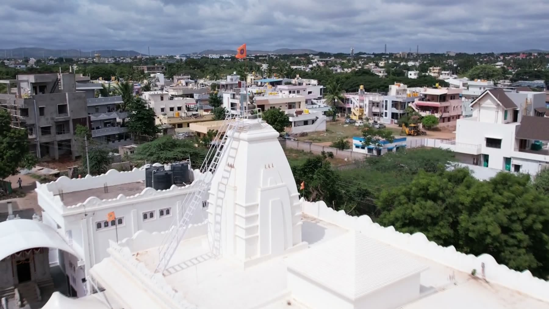 An aerial view looking down on the temple's white shikhara and terrace, with the rooftops of Gadag and distant hills stretching to the horizon.