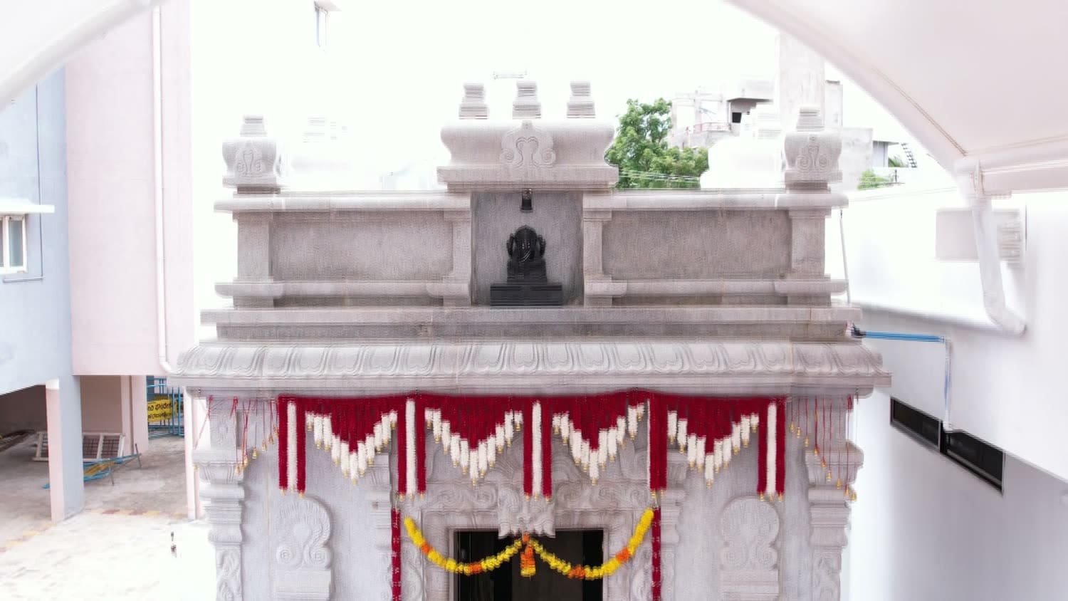 The Dwarakamai within the temple precinct: a carved stone shrine, its doorway hung with a marigold garland and red and white drapes.