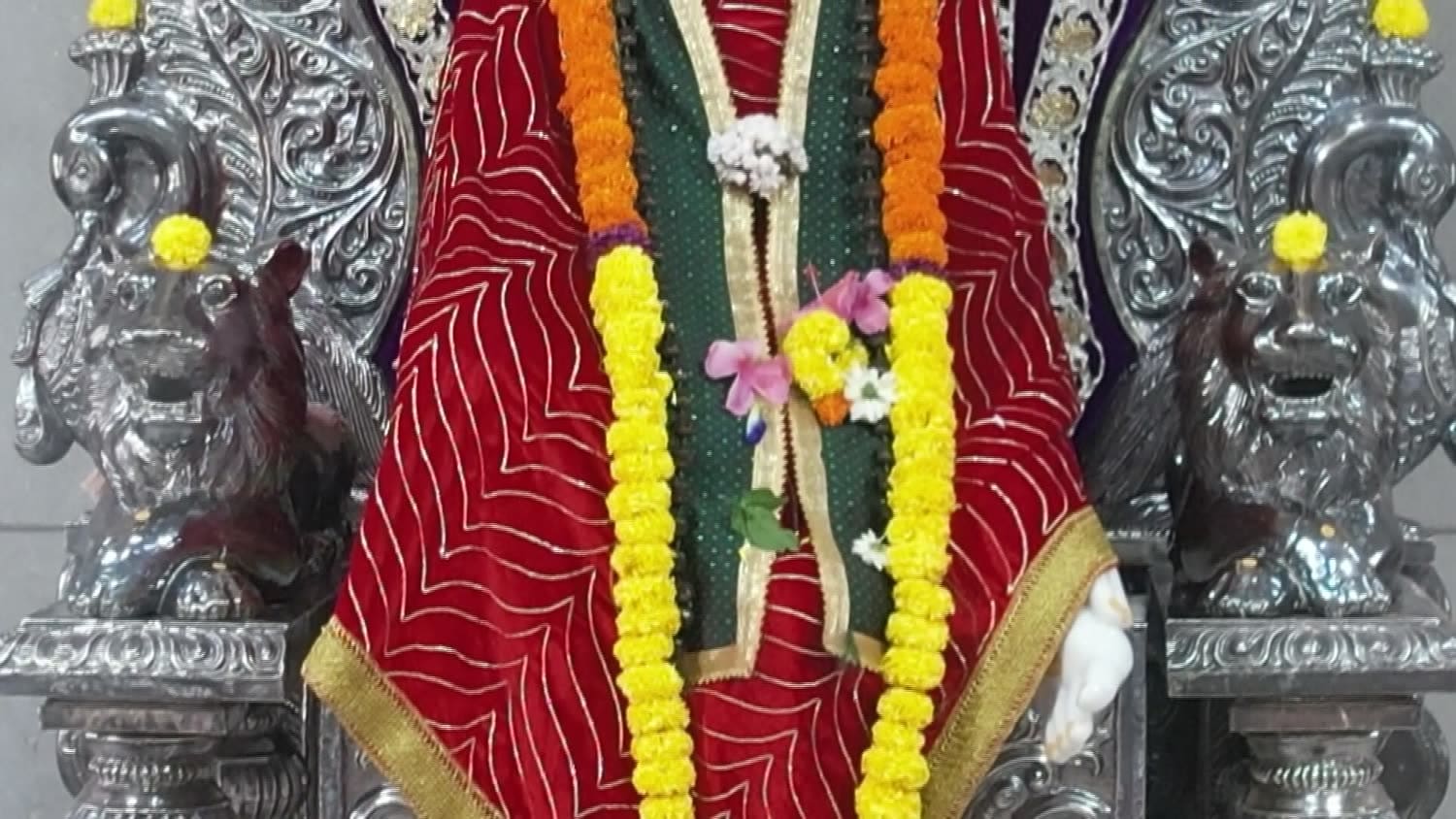Detail of marigold garlands laid over the murti's red robe, with carved silver columns on either side.