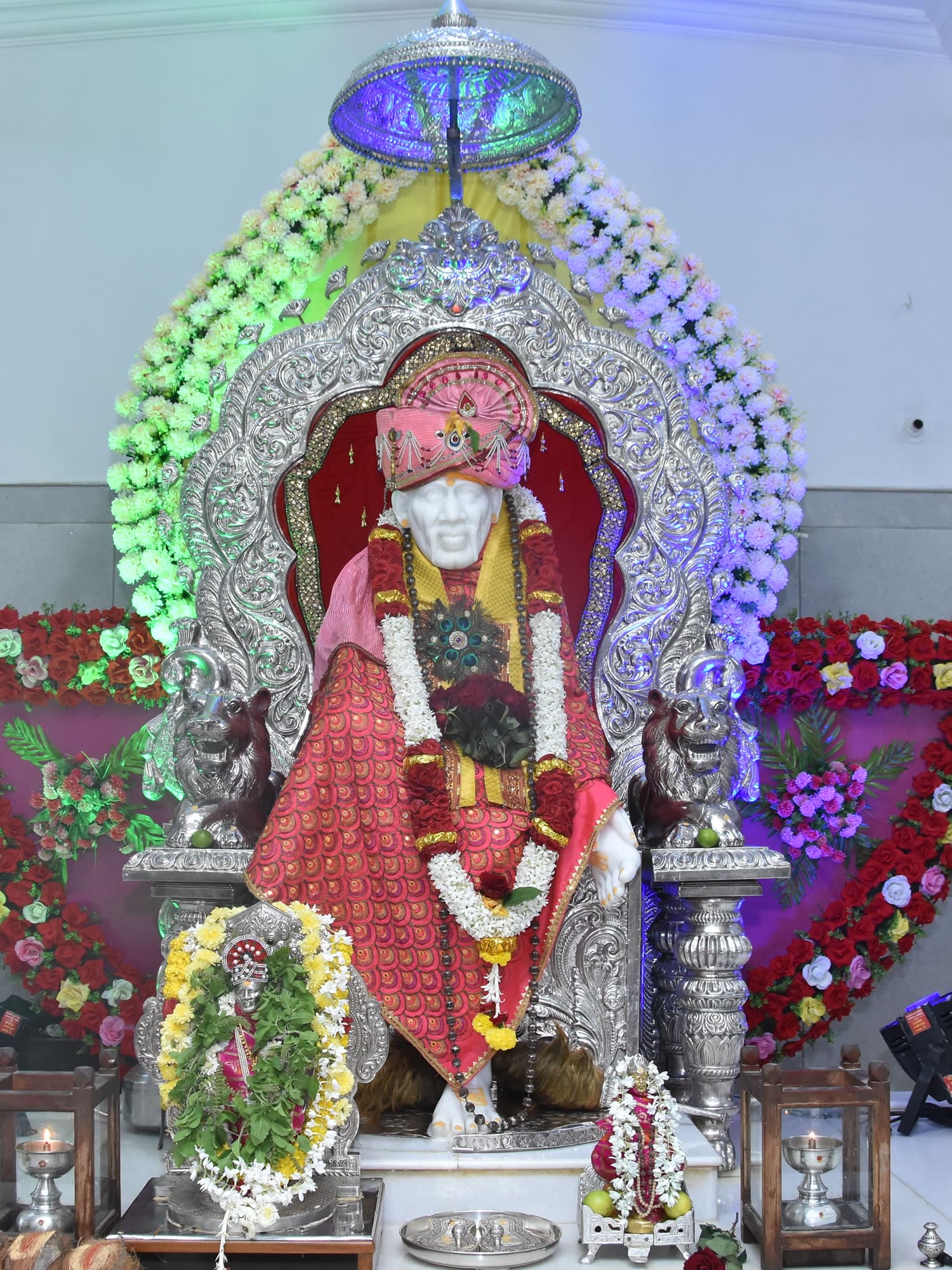 The murti beneath a tall arch of green and violet flowers.
