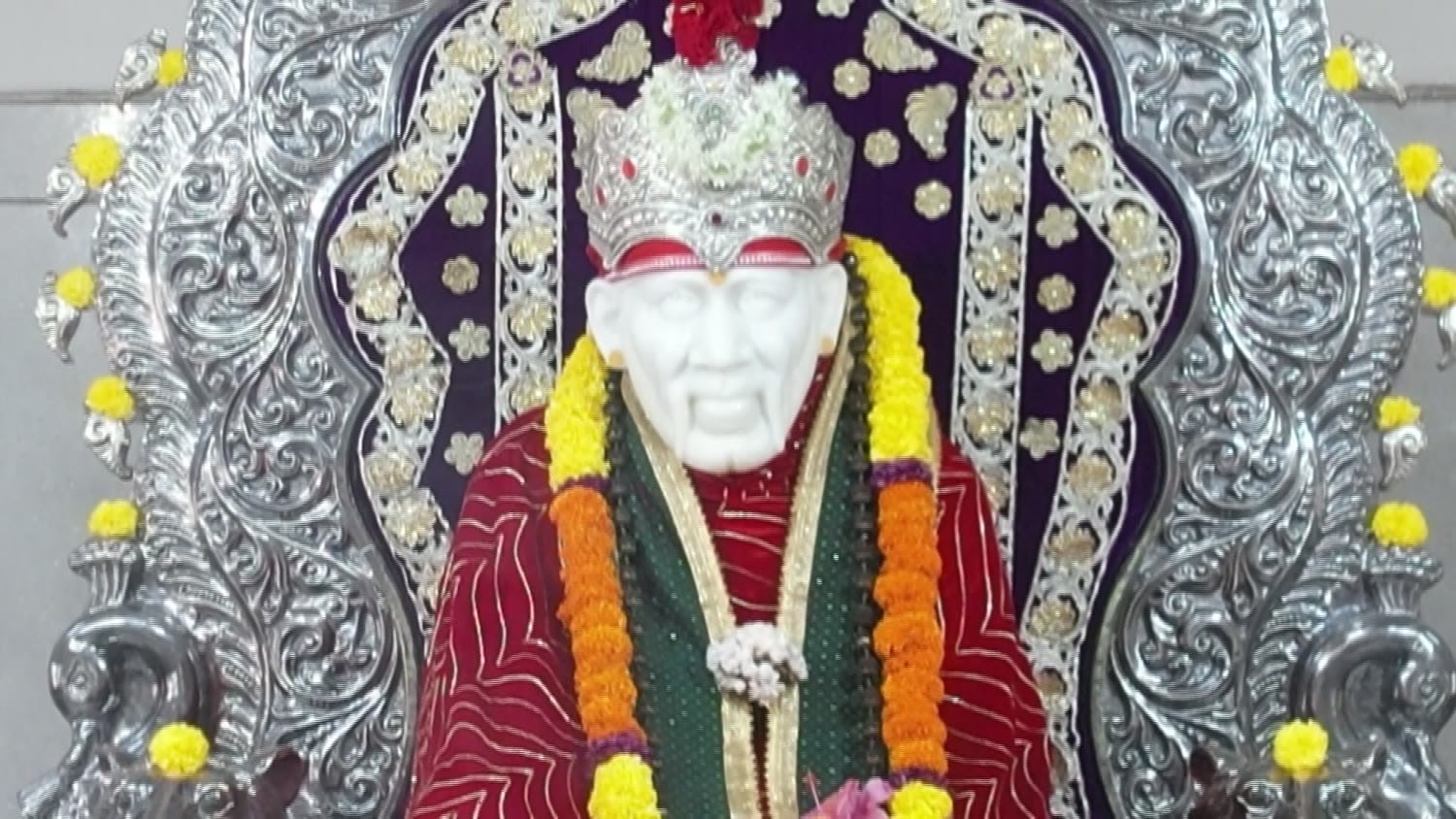 The murti of Shirdi Sai Baba, crowned and garlanded, seated within the silver prabhavali.