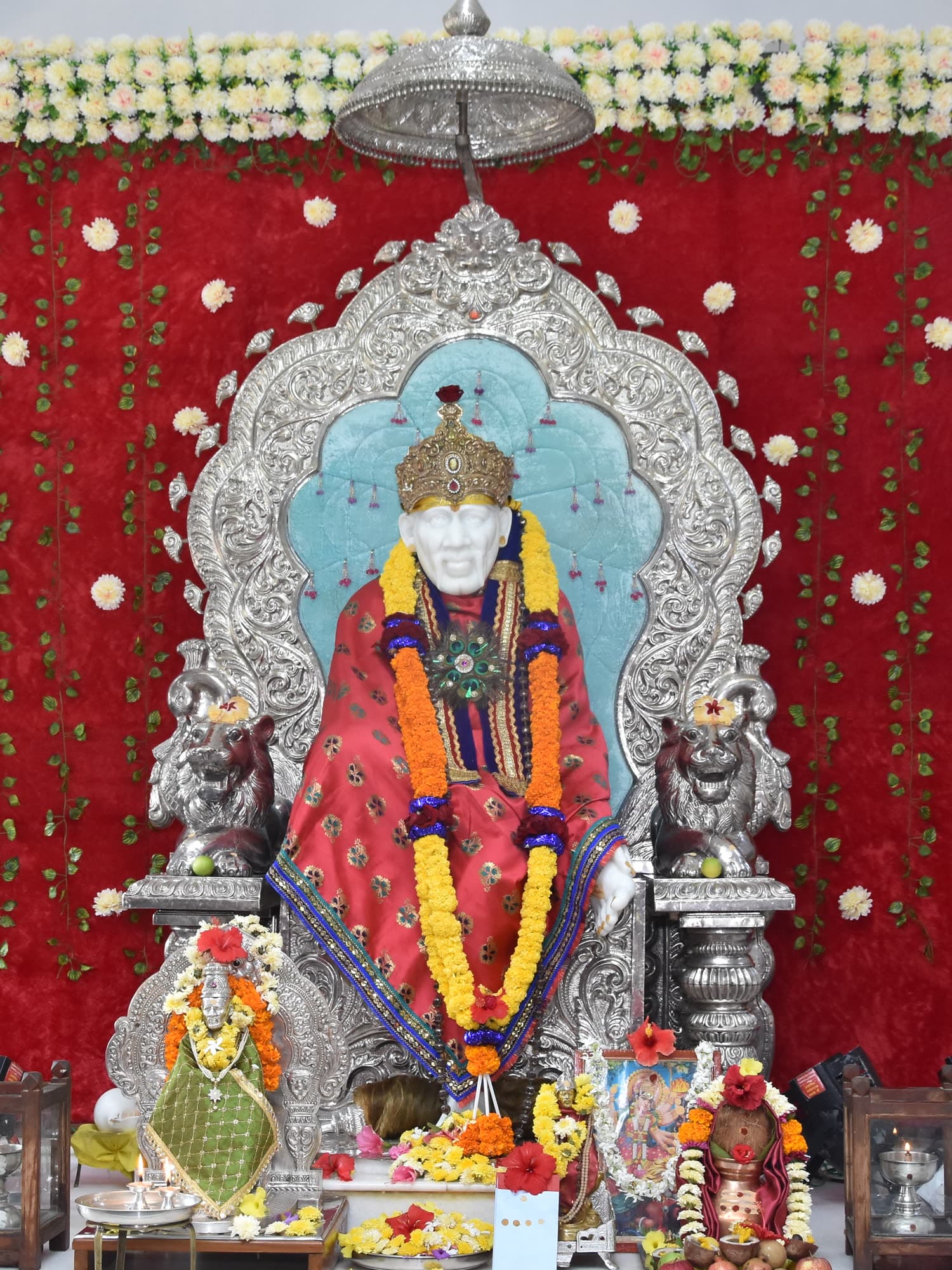 The murti before a crimson backdrop scattered with white flowers.