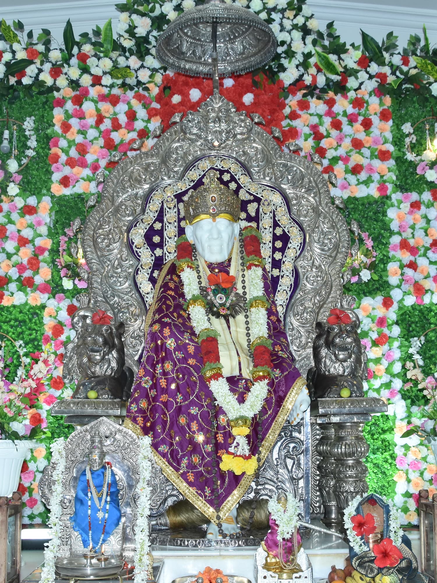 The murti framed by panels of green foliage interleaved with pink and white roses.