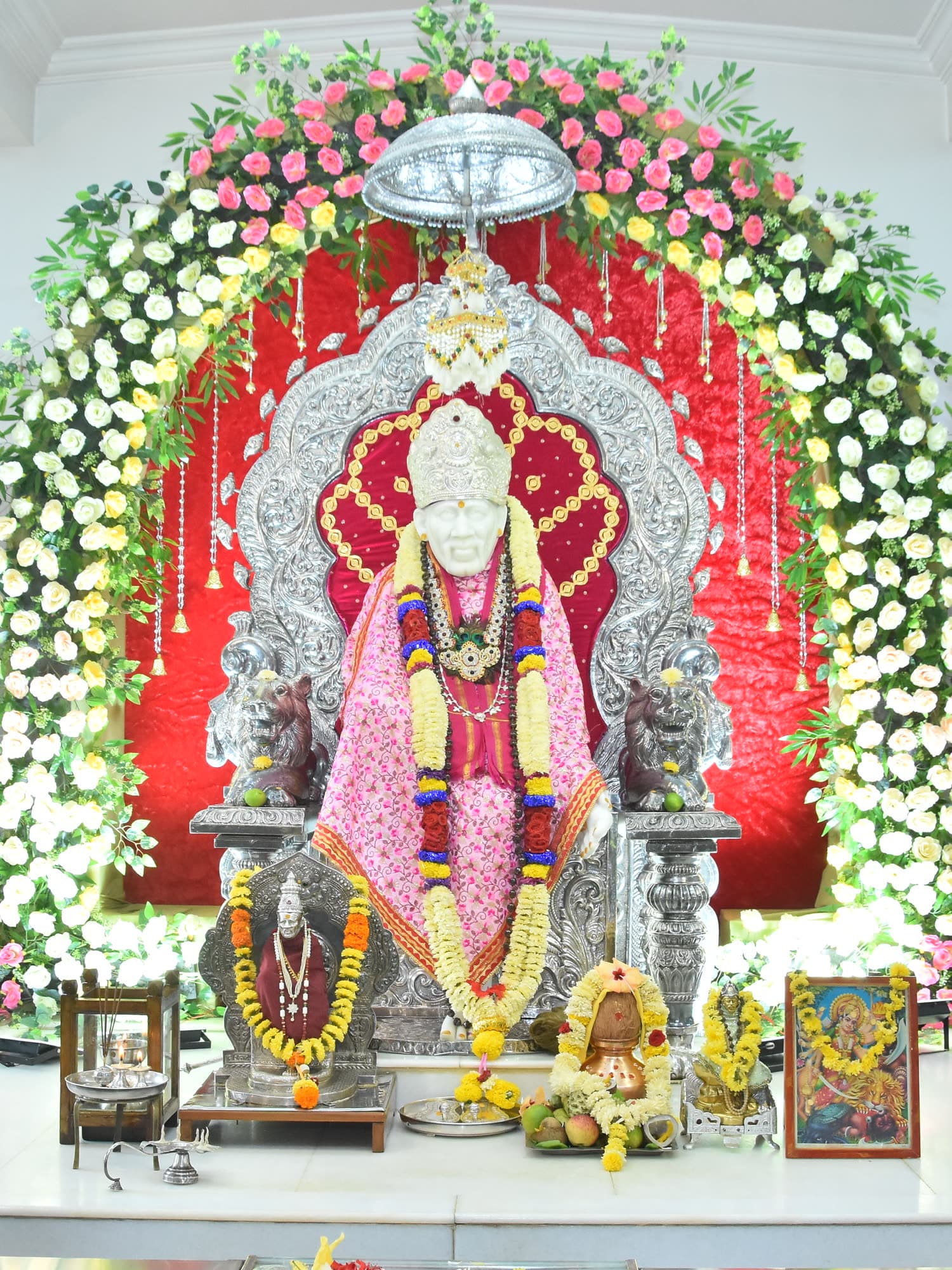 The murti in a pink robe beneath a canopy of rose and white flowers.