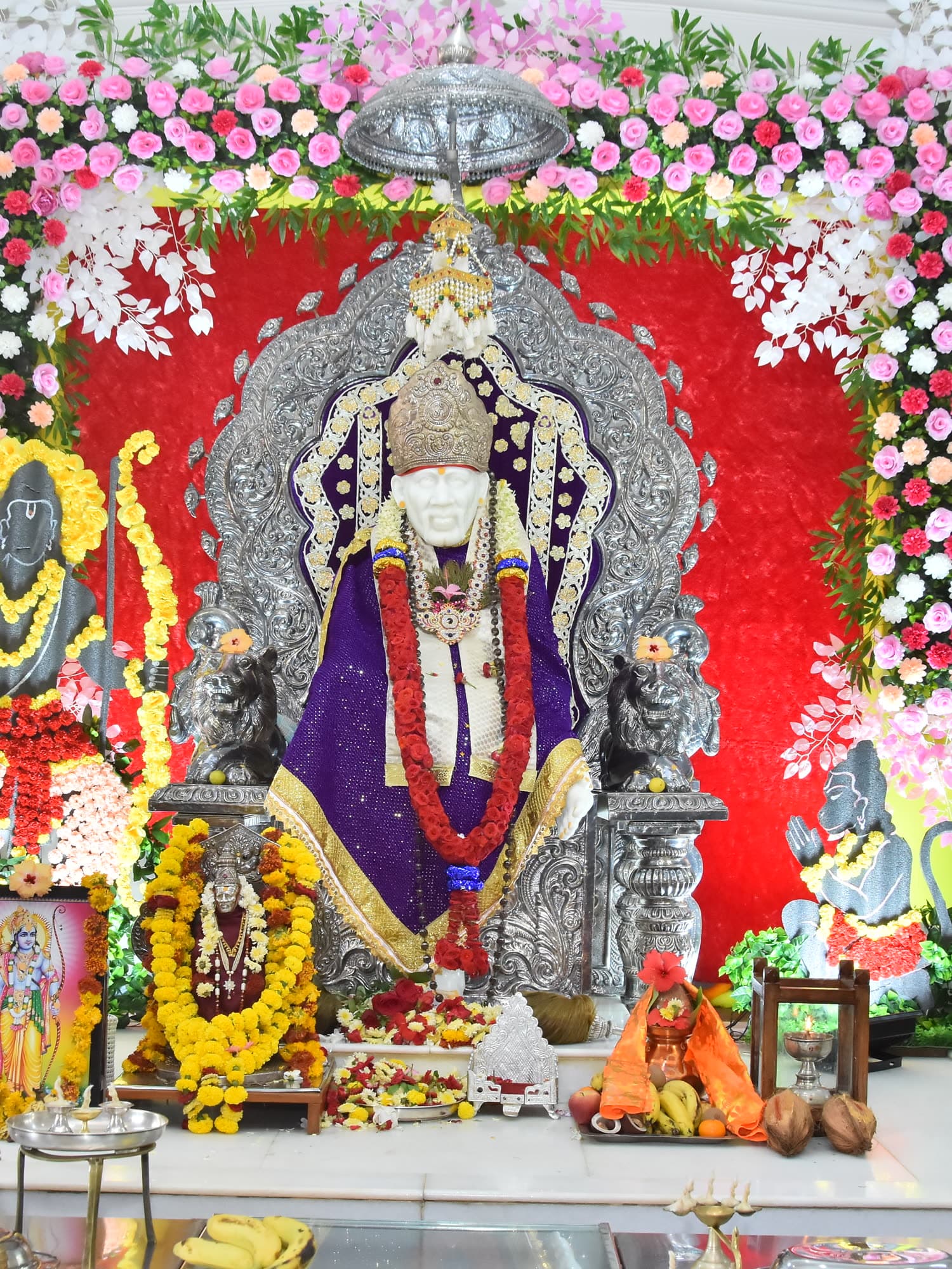 The murti in a violet and gold robe before a red backdrop.